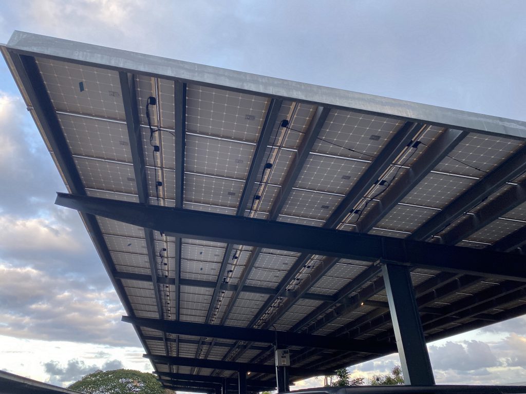 View from underneath of a commercial solar panel carport in a restaurant parking lot in Hawaii.